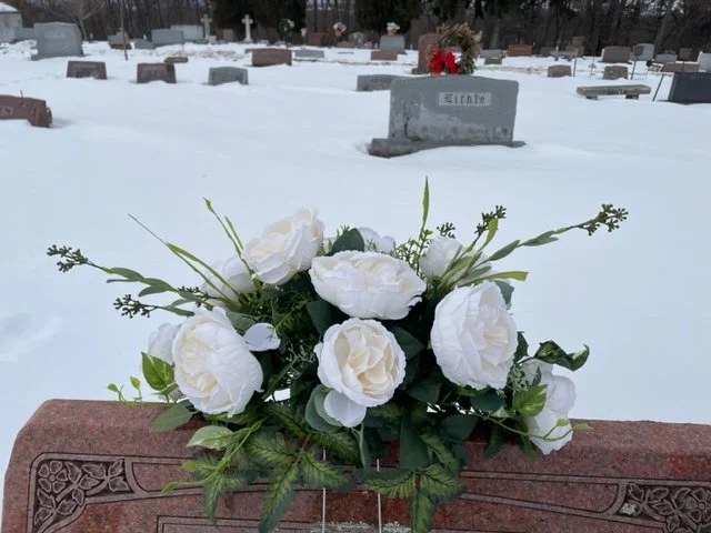 White roses and evergreen sprigs arranged on a real memorial in winter snow