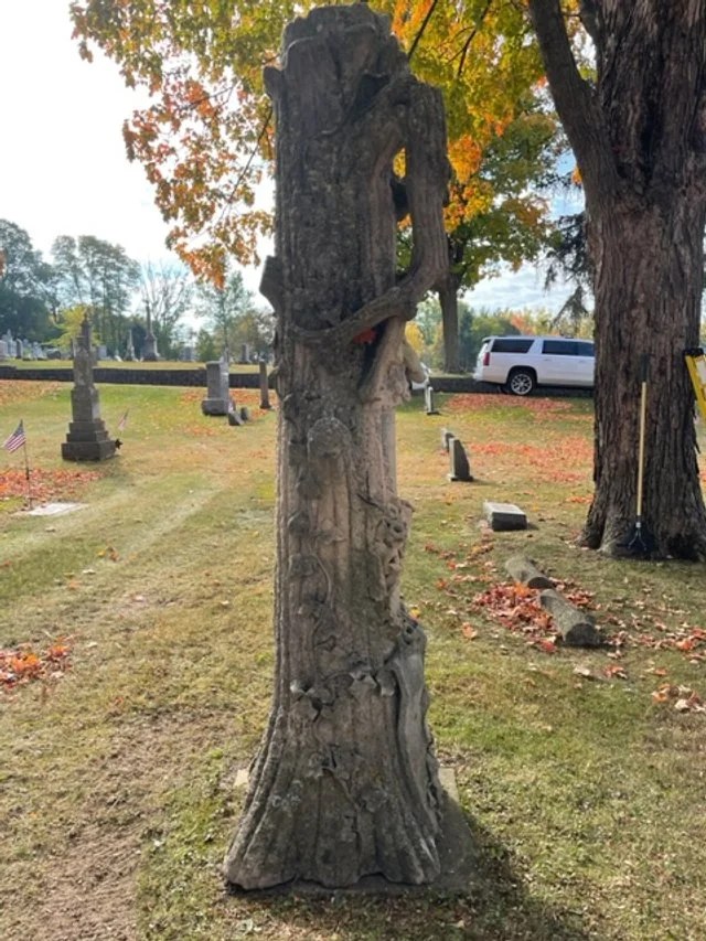 The Rathbun tree monument before restoration, with dark biological growth covering the sculpted trunk